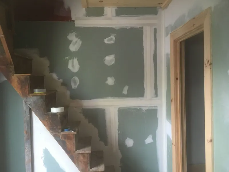 Drywall patches and taped seams along a stairwell wall before paint